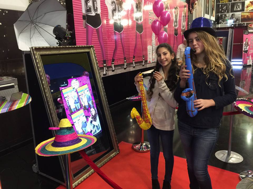 Girls interacting with mirror booth holding saxophones